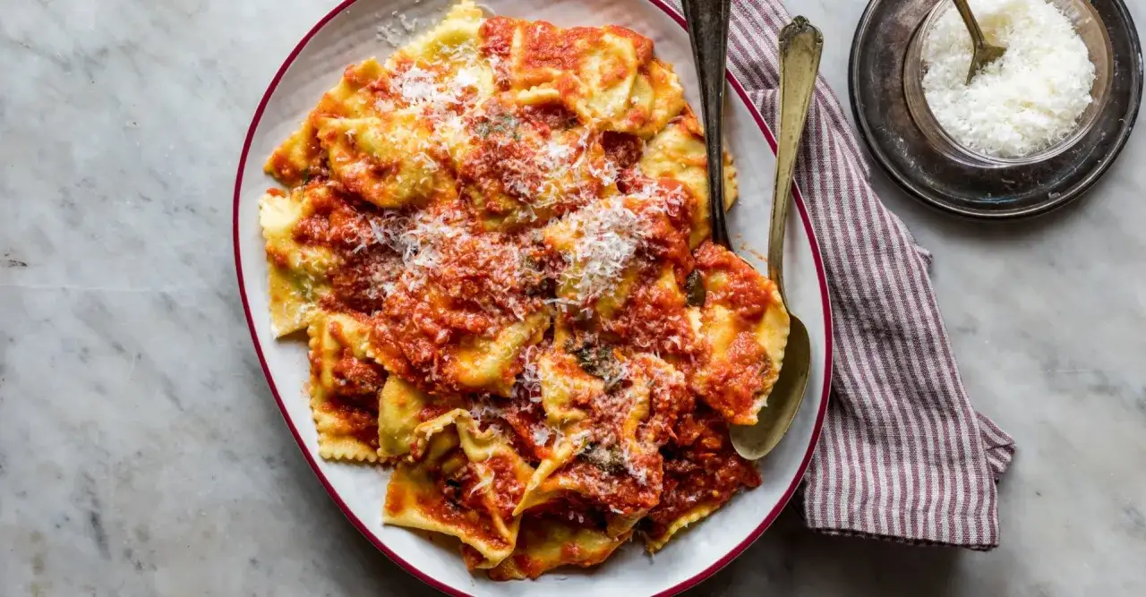Piatto di tortelli di patate ricetta toscana, conditi con sugo rosso e parmigiano grattugiato.