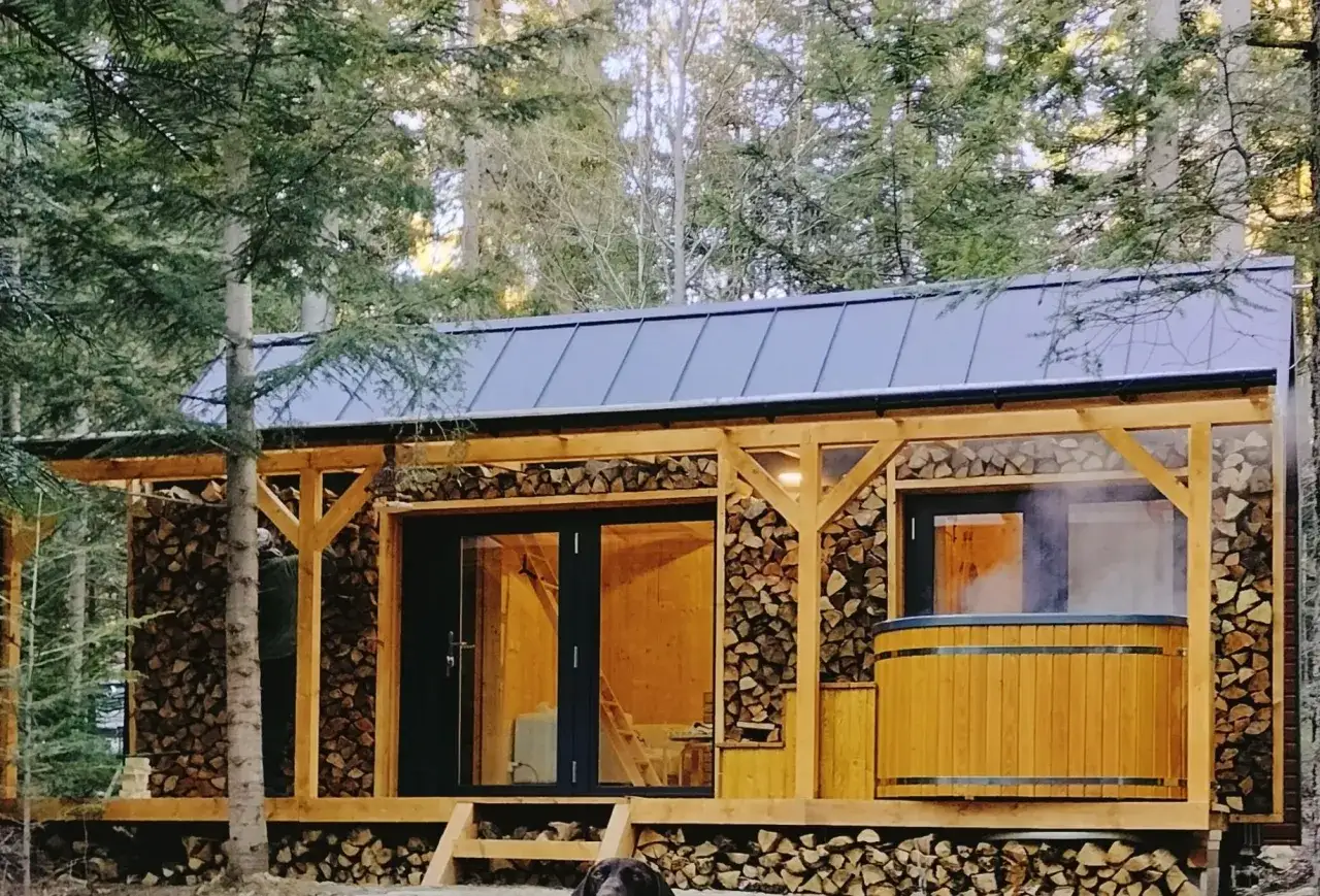 Uroczy tiny house Polska w otoczeniu lasu. Drewniana wanna z gorącą wodą paruje, zapraszając do relaksu.