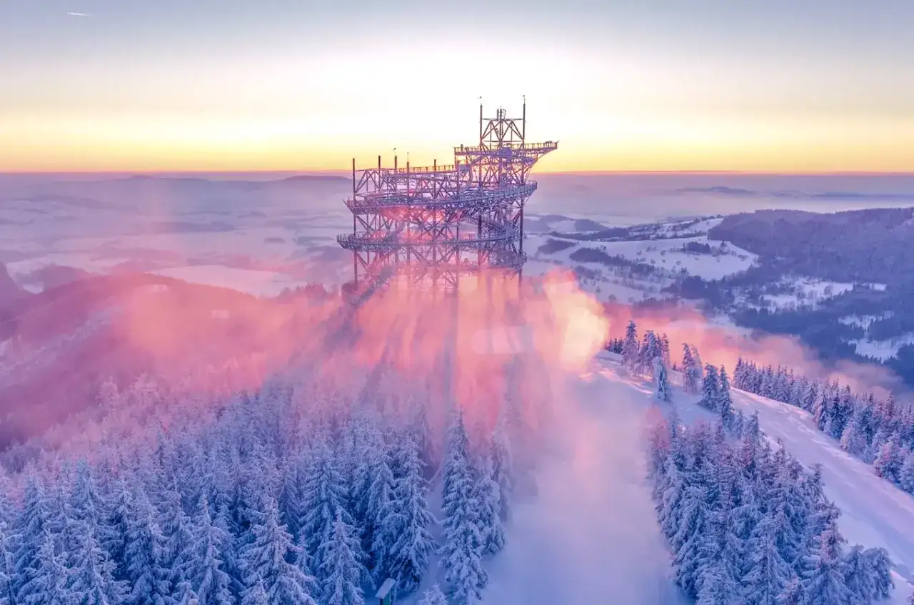 Widok na Sky Walk w Czechach o wschodzie słońca, otoczony ośnieżonymi drzewami i mgłą.