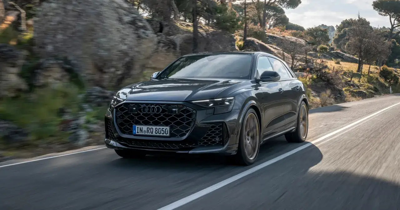 Czarny Audi RS Q8 pędzi po krętej drodze wśród skał i drzew. Sprawdź aktualną audi rsq8 cena.