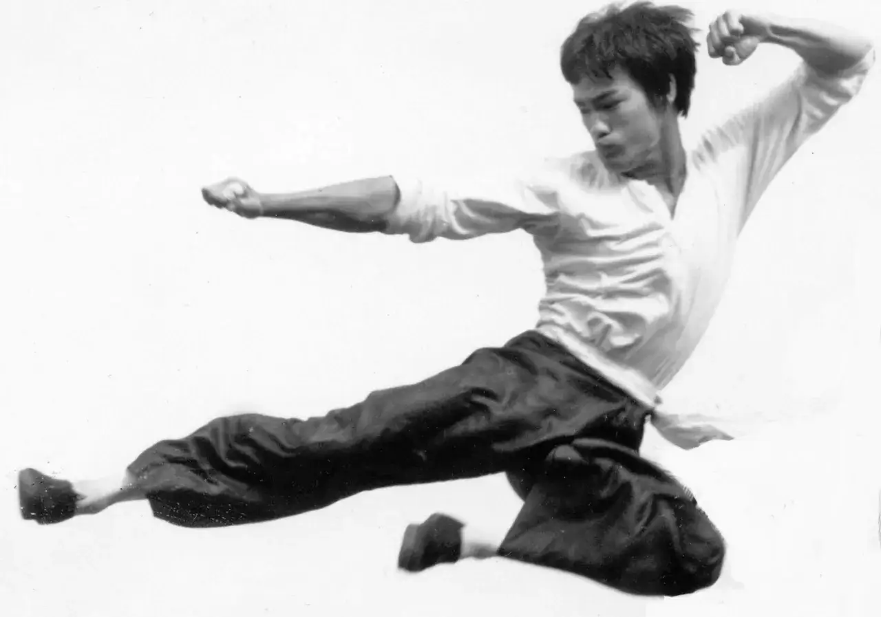 Bruce Lee i luften, utf&ouml;r en spark i sin ikoniska jeet kune do-stil.