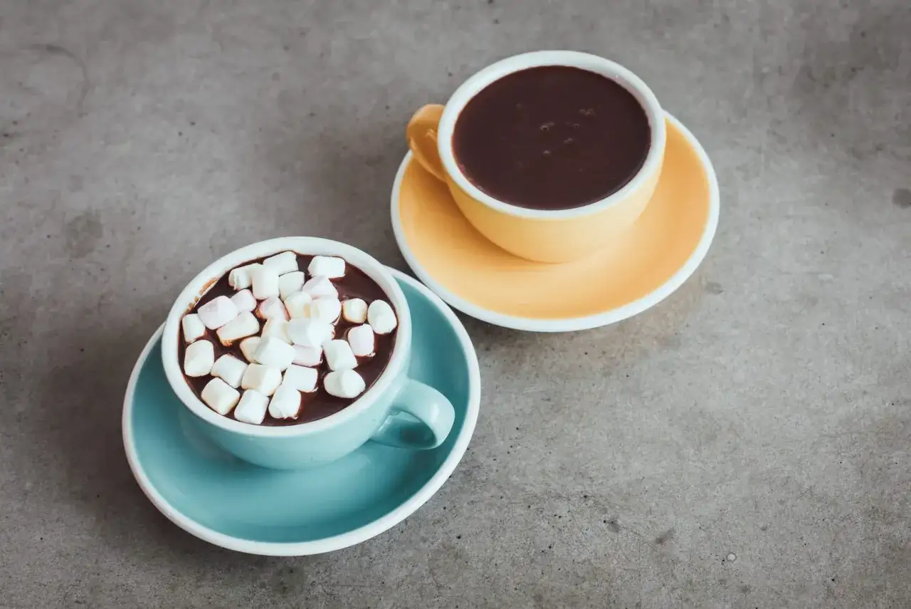 Dwie filiżanki gorącej czekolady do picia: jedna z piankami marshmallow, druga bez. Idealne na zimowe wieczory.