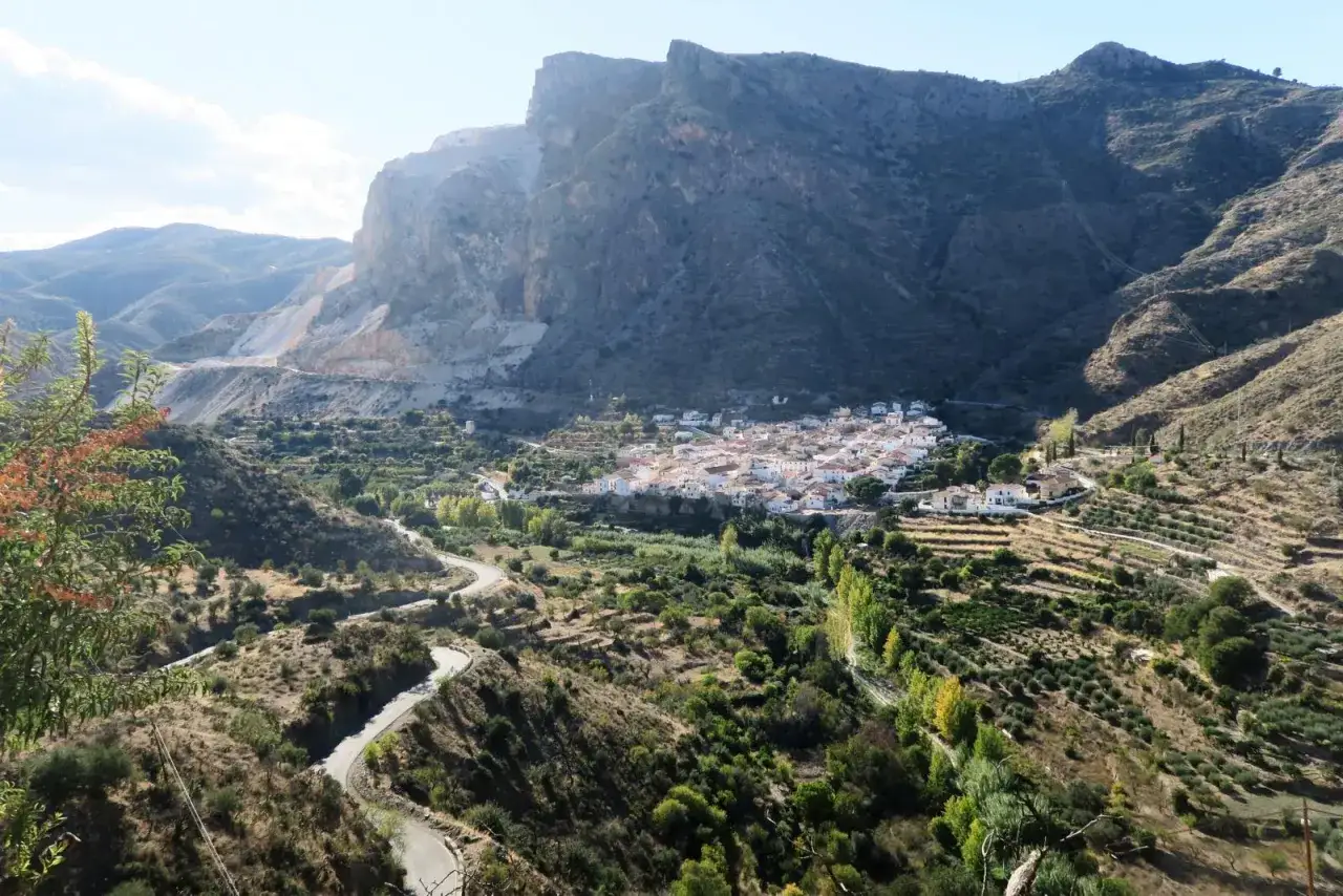 Pueblo blanco en la **sierra de los Filabres**, rodeado de vegetaci&oacute;n y olivos, con una carretera serpenteante y una cantera en la monta&ntilde;a.