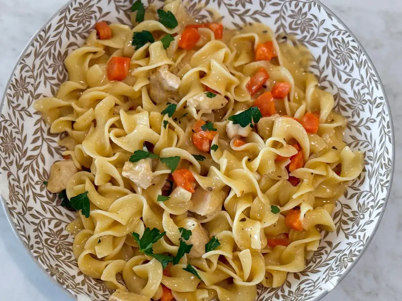 Herzhafte nudeln mit ei, H&uuml;hnchen und Karotten in einer cremigen Sauce, garniert mit Petersilie.