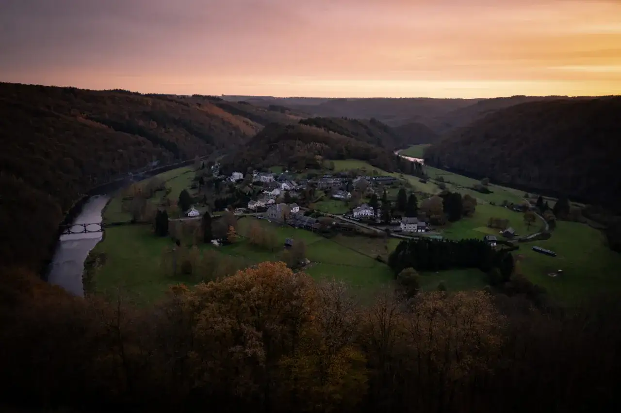 Vue aérienne d'un village niché dans une vallée verdoyante, traversée par une rivière. Parfait pour une randonnée à Bouillon.