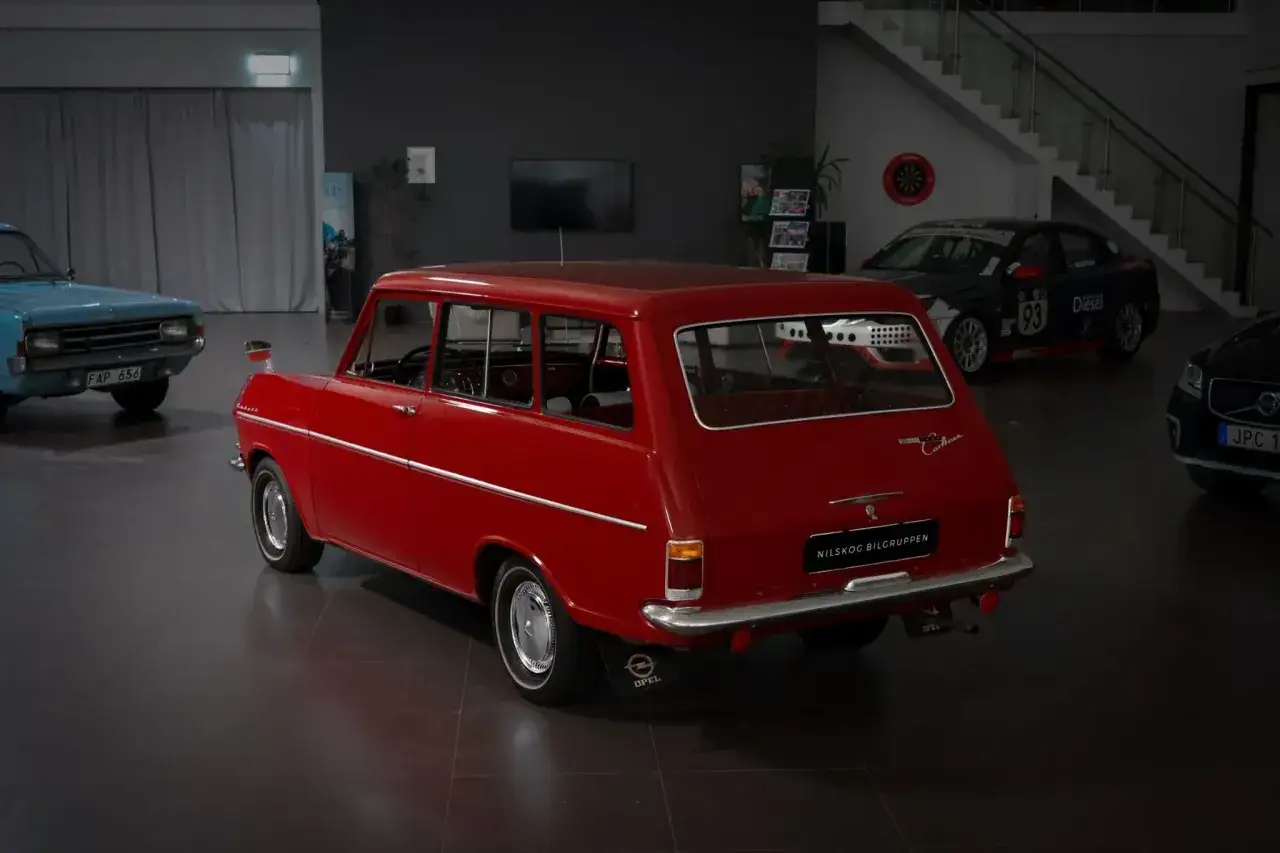 Röd Opel Caravan, en klassisk skattebefriad bil, står i en bilhall bredvid en blå och en svart bil.