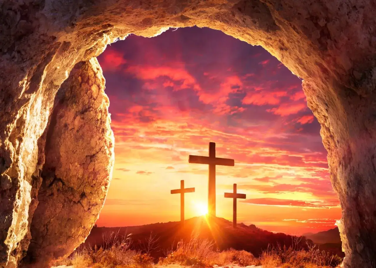 Three crosses stand on a hill against a vibrant sunset, viewed from inside a cave. This scene embodies the gospel of Jesus Christ, symbolizing hope and redemption.
