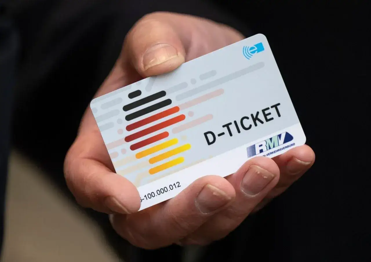Hand hält Deutschlandticket NRW. Das Ticket zeigt die deutsche Flagge und das Logo des RMV-Verkehrsverbunds.