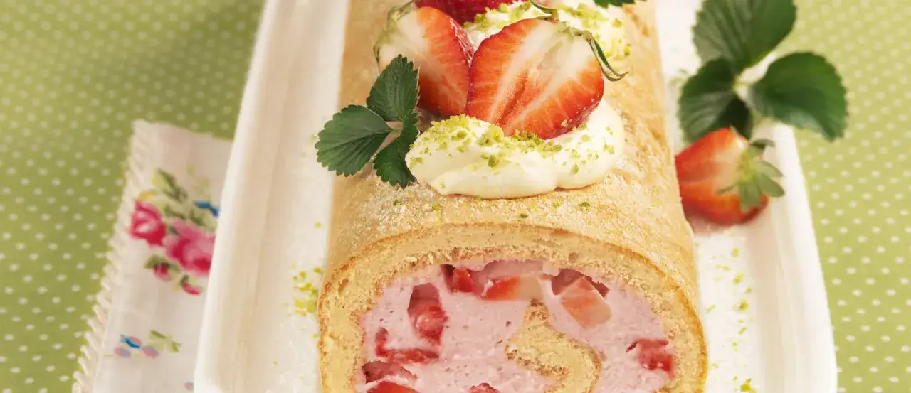 Saftige Erdbeer-Biskuitrolle mit Sahne und frischen Erdbeeren, bestreut mit Pistazien. Ein Genuss für jeden Anlass.