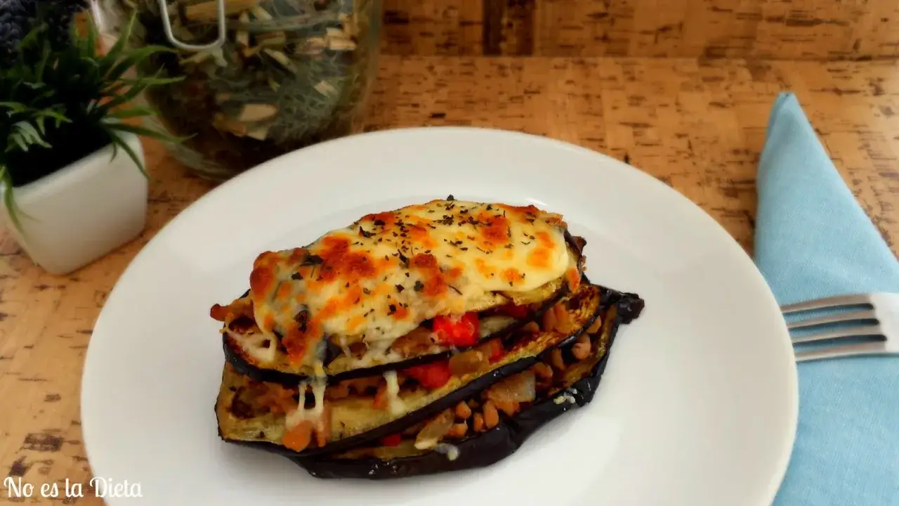 Lasaña de berenjena gratinada, con capas de verduras y queso derretido, servida en plato blanco.