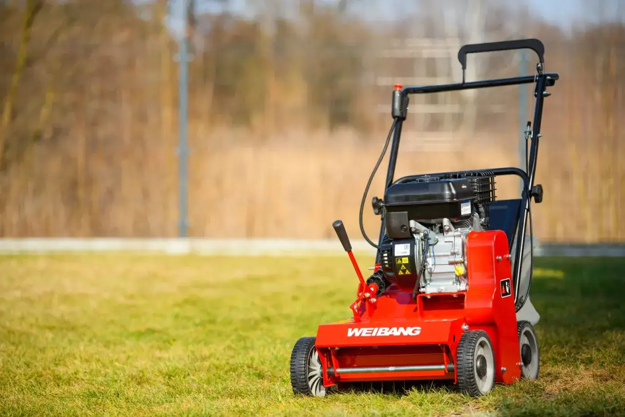 Czerwony aerator do trawnika Weidemann gotowy do pracy na zielonej murawie.