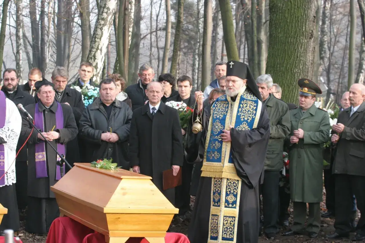 Uroczystość pogrzebowa w cerkwi. Duchowny w ozdobnej szacie prowadzi obrzęd przy trumnie.