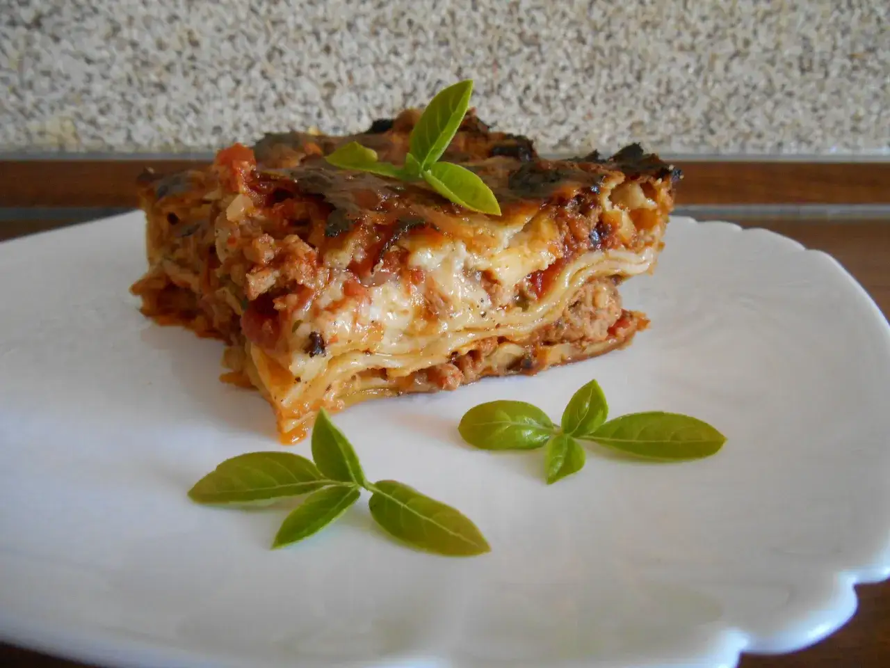 Pyszna lasagna z mięsem mielonym, idealna odpowiedź na pytanie co ugotować z mięsa mielonego. Udekorowana listkami bazylii.