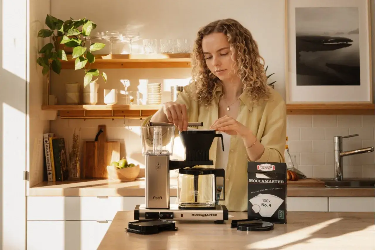 En kvinna f&ouml;rbereder kaffe med en Moccamaster. Hon funderar p&aring; hur m&aring;nga skopor kaffe till 2 koppar.