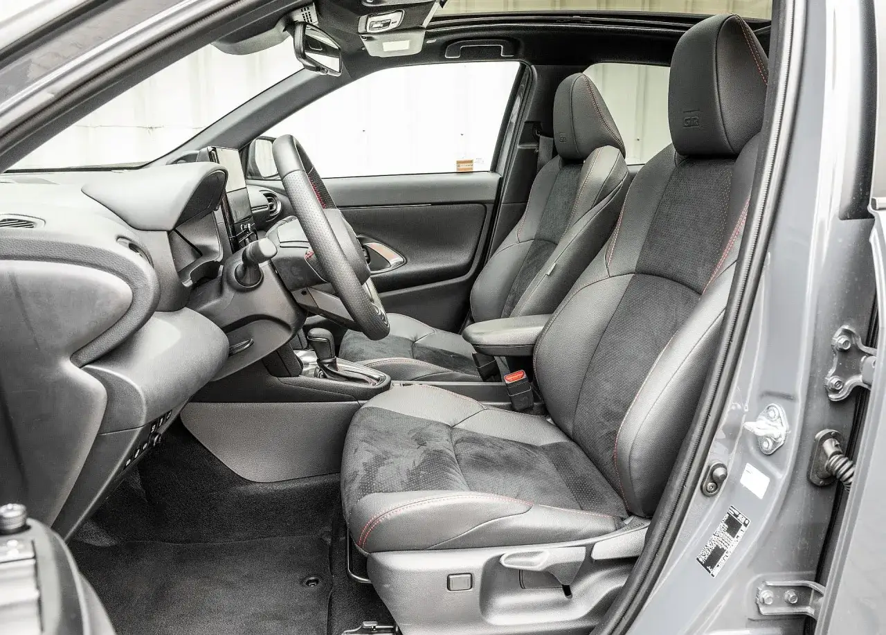 Wnętrze Toyota Yaris Cross 2025 z czarnymi fotelami i czerwonymi przeszyciami. Widoczny fragment deski rozdzielczej i kierownicy.
