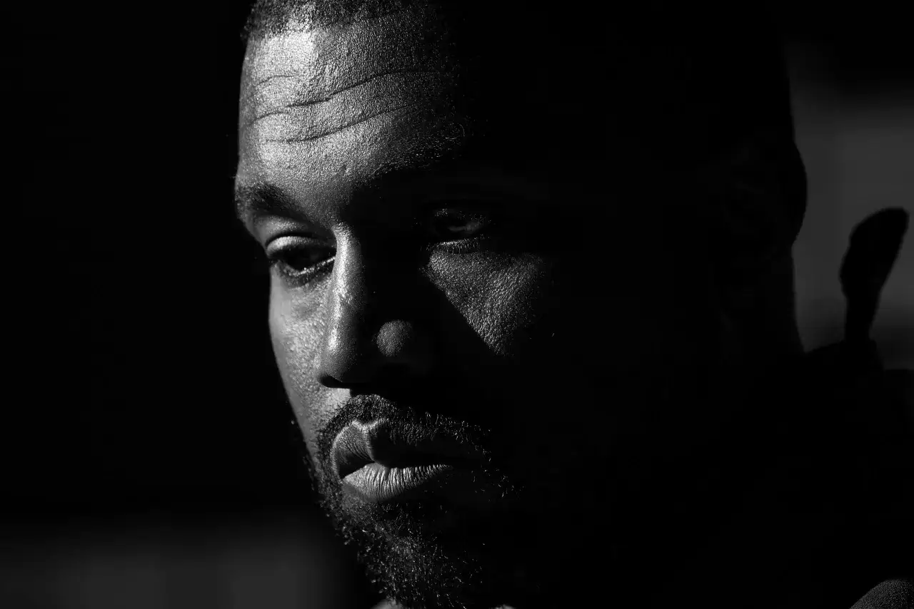 Zbliżenie na twarz Kanye Westa, z wyraźnie zaznaczonymi zmarszczkami na czole i błyszczącą skórą.