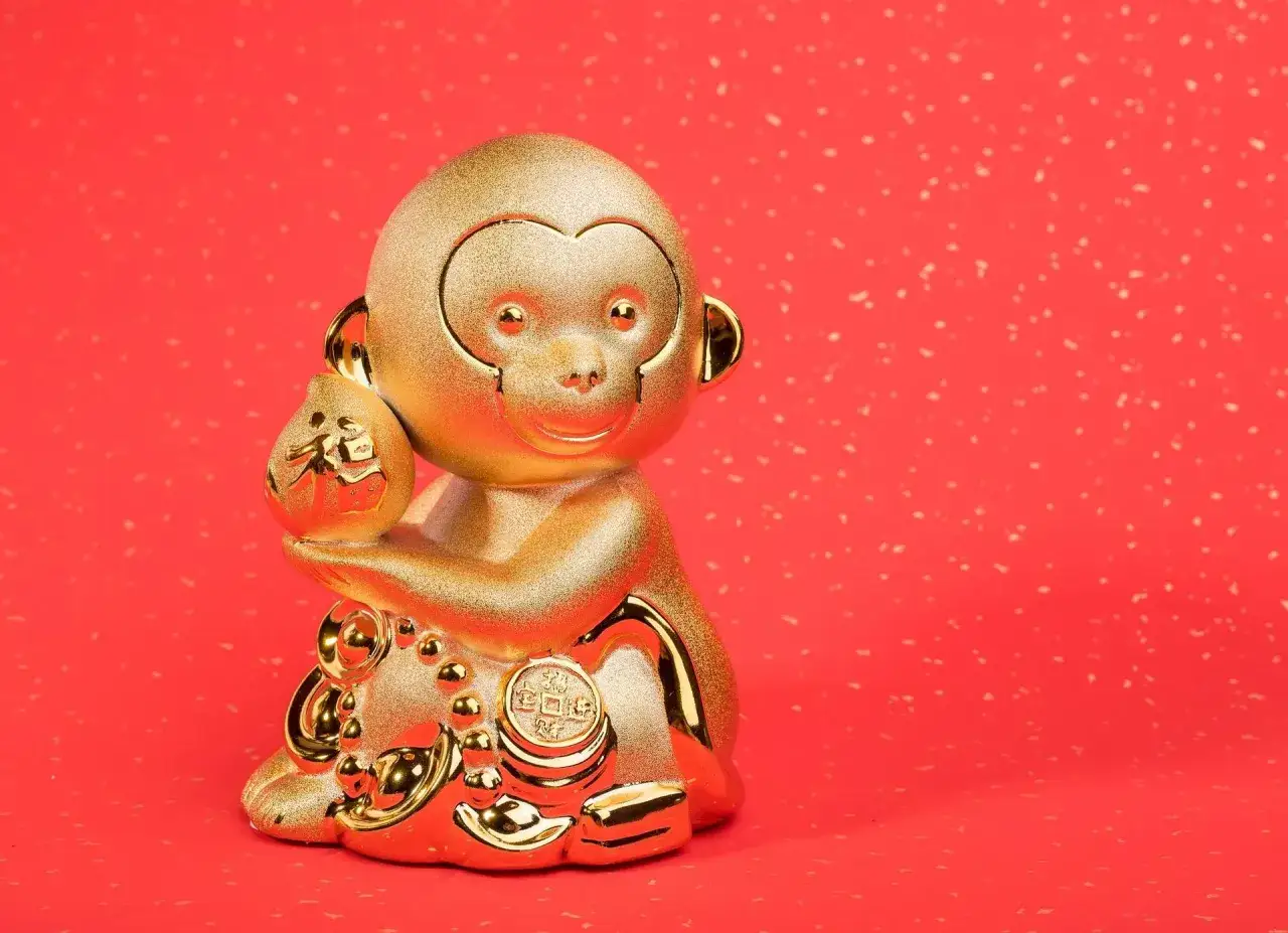 Złota figurka małpy, chiński znak zodiaku, trzymająca woreczek z symbolem szczęścia.