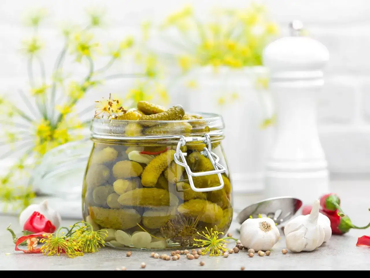 Słoik pełen chrupiących og&oacute;rk&oacute;w po kartusku, otoczony czosnkiem, chili i koprem. Idealne na letnie przetwory.