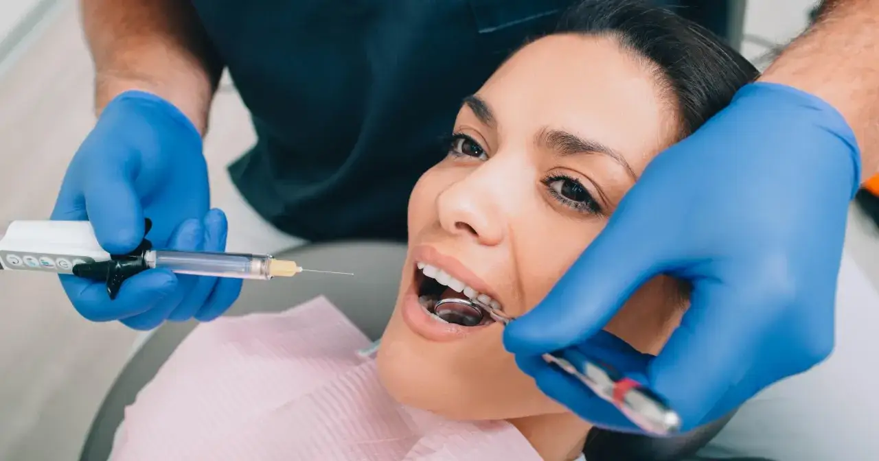 Dentysta podaje znieczulenie, by bez bólu usunąć próchnicę. Pacjentka patrzy z nadzieją na zdrowy uśmiech.