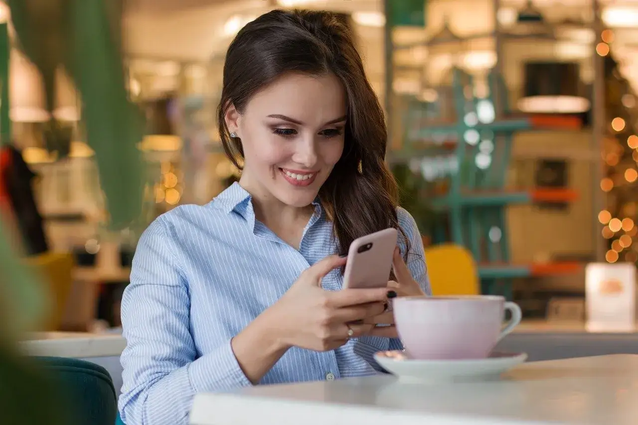 Uśmiechnięta dziewczyna czyta pierwszą wiadomość na Tinderze, trzymając w dłoniach telefon.