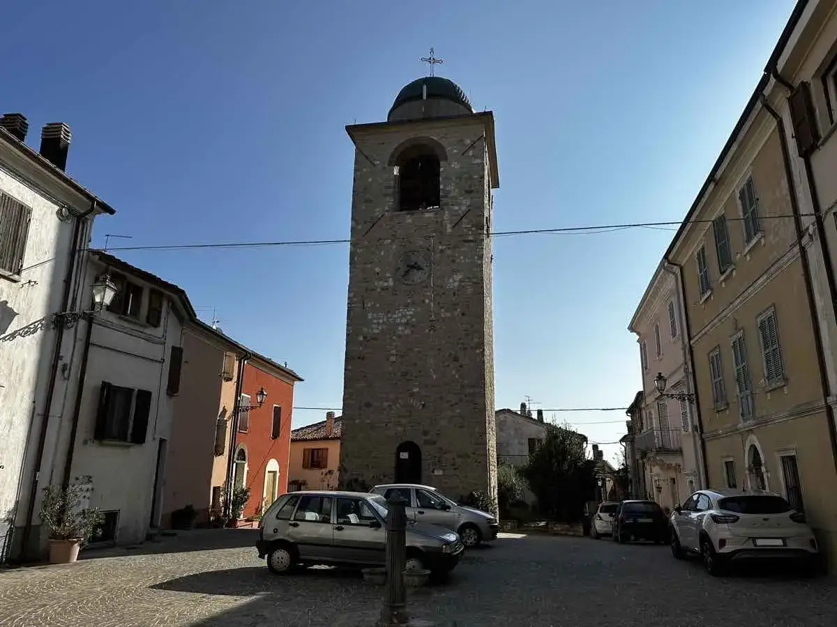 Torre campanaria nel borgo di Monte Grimano, con case colorate e auto parcheggiate.