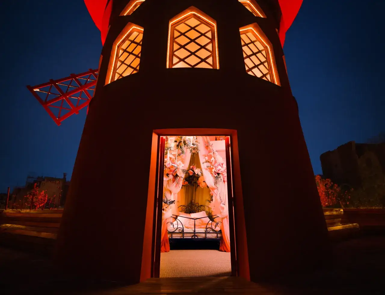 Le Moulin Rouge de Paris s'illumine la nuit, révélant une chambre décorée de fleurs et de voilages roses, invitant à la rêverie.