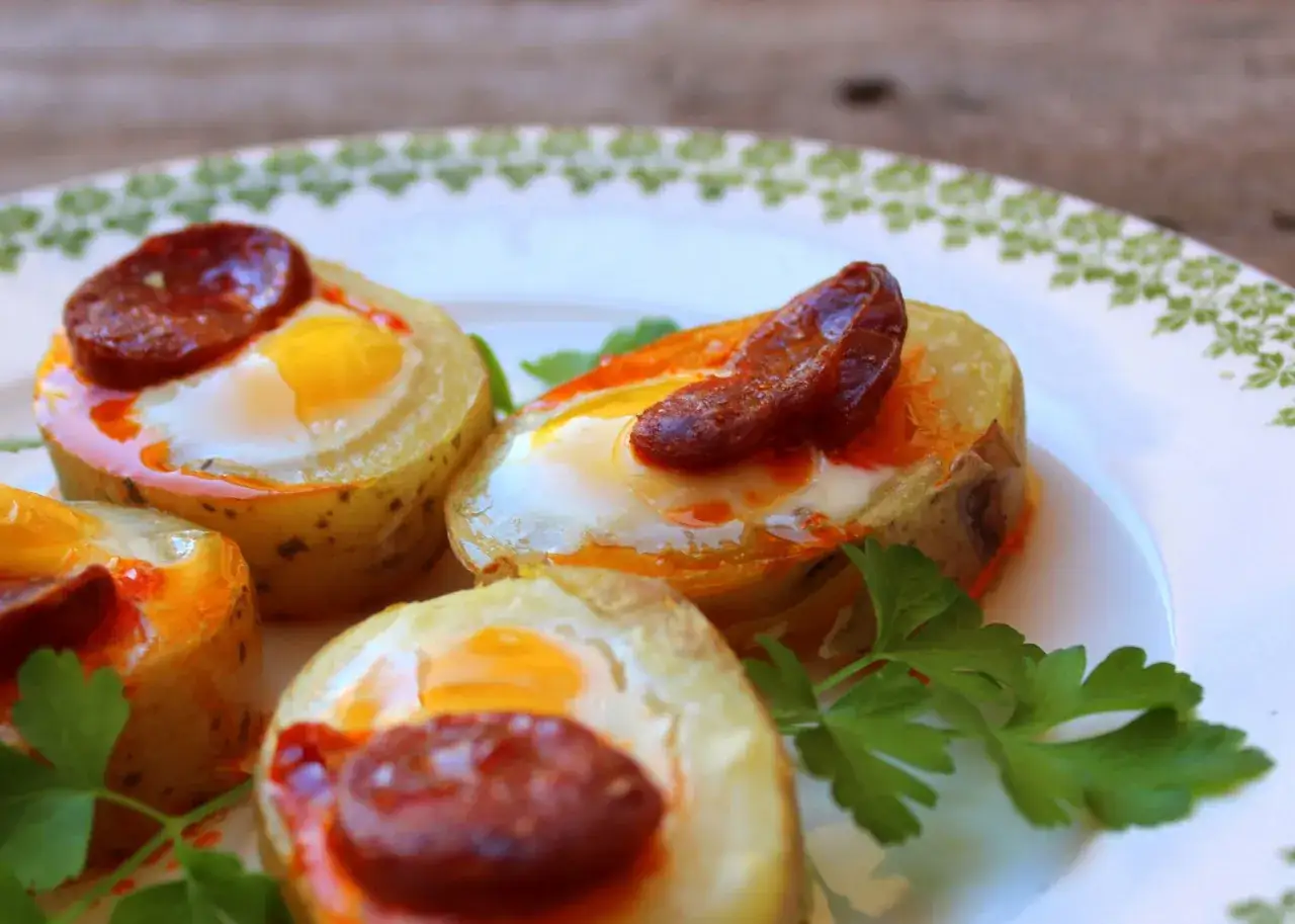 Canapés con huevos de codorniz y chorizo, servidos en rodajas de patata horneada, decorados con perejil fresco.