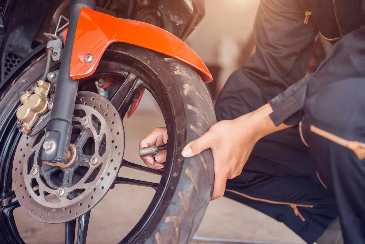 Mechanik sprawdza ciśnienie w oponie motocykla. Dowiedz się, jaka jest wymiana opon w motocyklu cena.