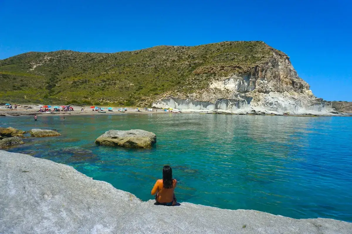 Frauen sitzen am Ufer der playa de los genoveses, blicken auf das t&uuml;rkisfarbene Meer und die felsige K&uuml;ste.