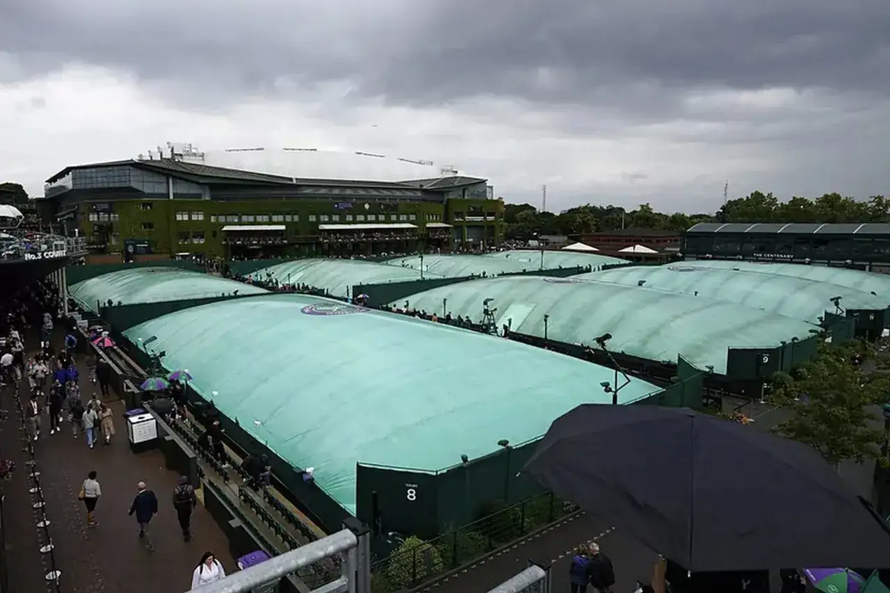 Wimbledon deszcz. Trybuny i korty tenisowe przykryte zielonymi płachtami, ludzie z parasolami.