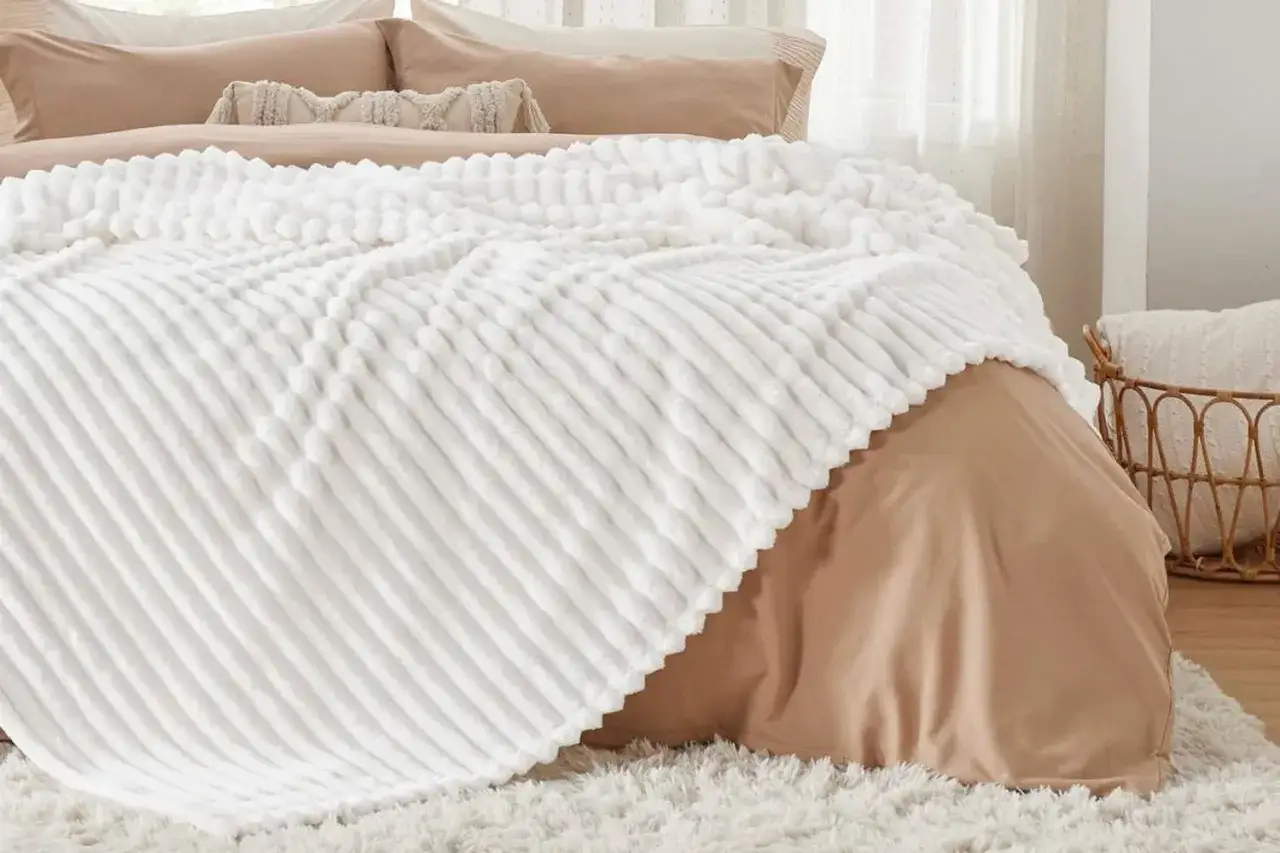 A plush white throw blanket with a ribbed texture is draped over a bed. Wondering if you can wash a throw blanket like this? Yes, this cozy blanket is machine washable.