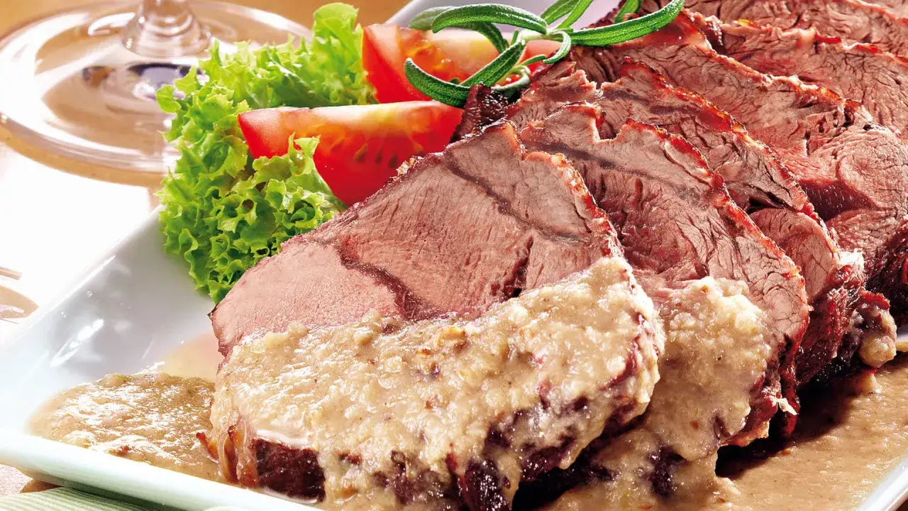Saftiger Sauerbraten mit Sauce, garniert mit Salat und Tomaten. Die Marinierzeit beeinflusst, wie lange man Sauerbraten einlegen kann.