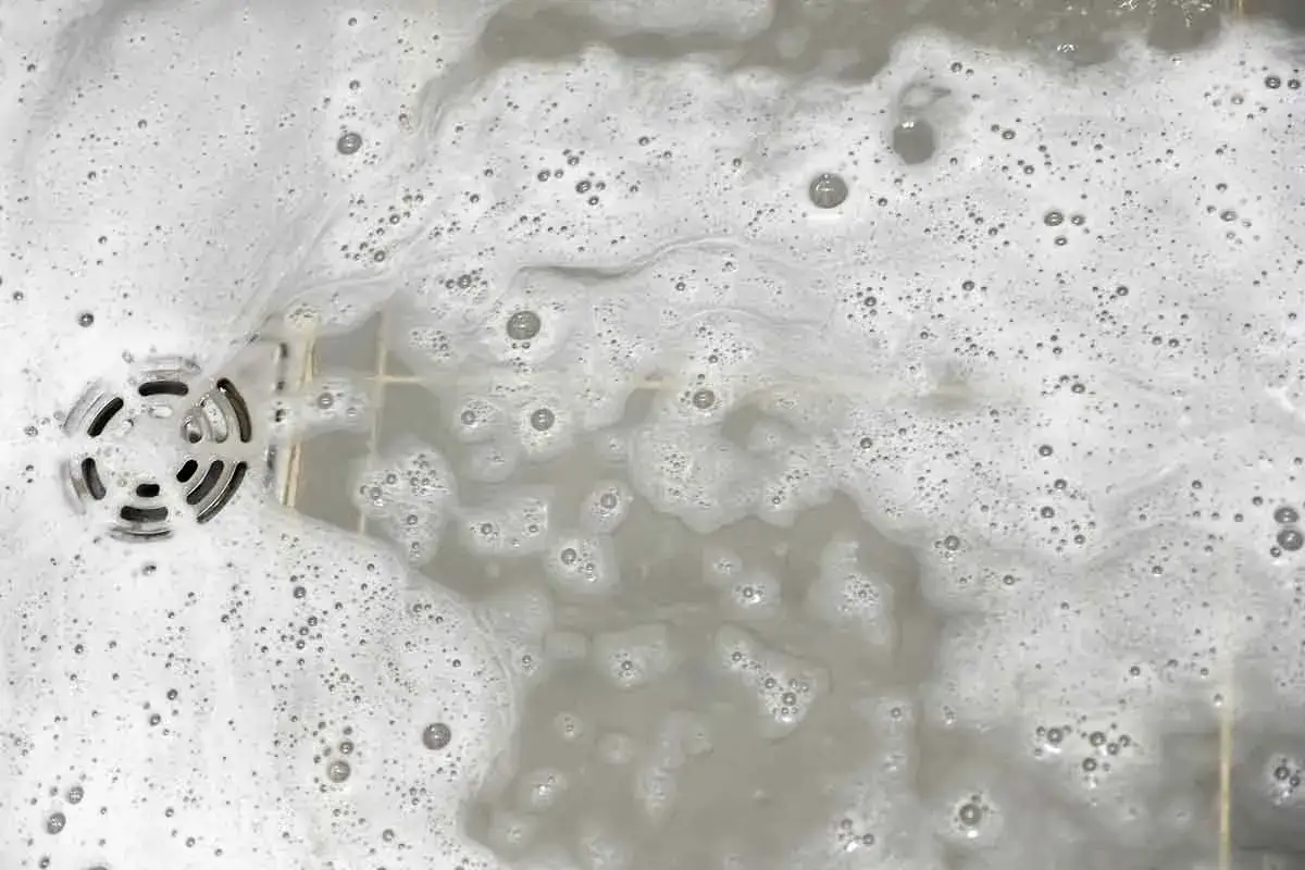 Schiuma e bolle coprono lo scarico della doccia, suggerendo che il suo scarico doccia puzza e necessita di pulizia.