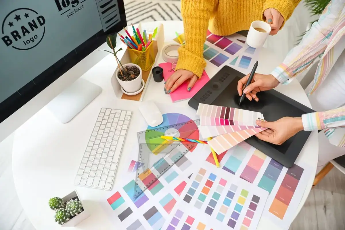 Cr&eacute;ation de logos et identit&eacute;s visuelles : un m&eacute;tier artistique bien pay&eacute;. Des designers travaillent sur des palettes de couleurs et des tablettes graphiques.