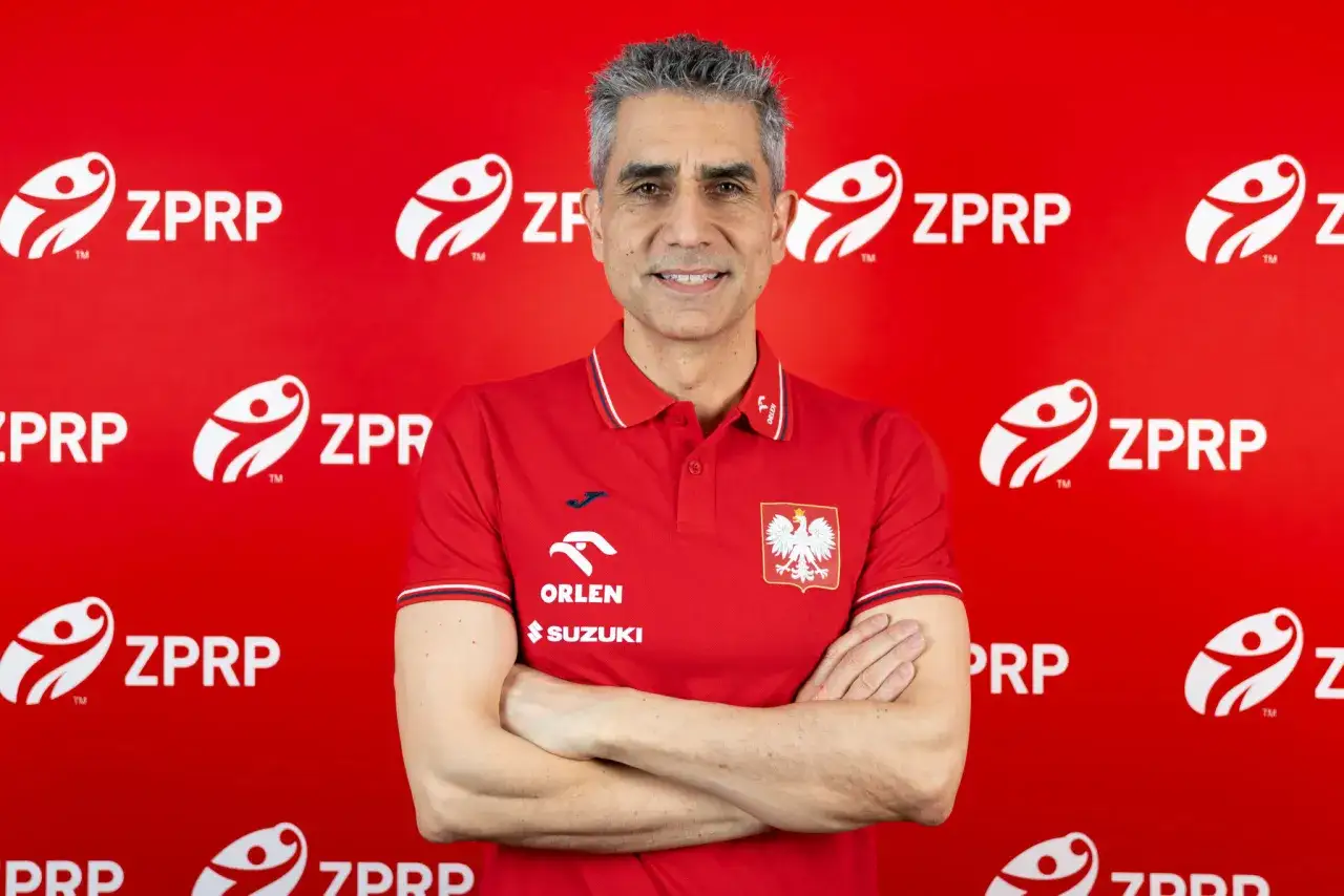 Trener reprezentacji Polski w piłce ręcznej, w czerwonej koszulce z orłem, na tle z logo ZPRP.