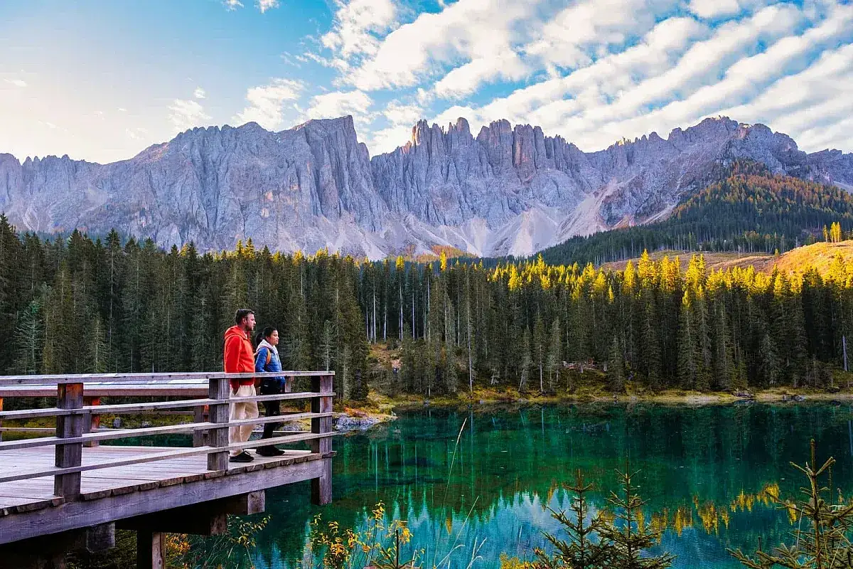 Coppia ammira la bellezza dei laghi nord Italia, con montagne maestose e foreste di conifere che si specchiano nelle acque cristalline.