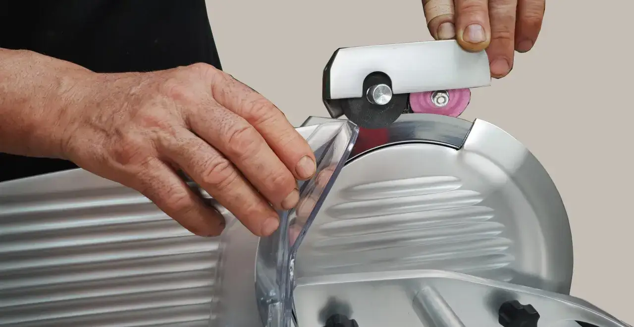 Mani che affilano la lama di un'affettatrice. Un accessorio per affilare viene usato per mantenere la lama in perfette condizioni, essenziale per sapere come pulire affettatrice e mantenerla efficiente.