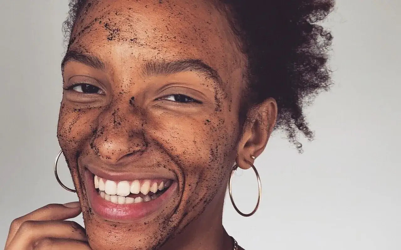 Donna sorridente con maschera scrub sul viso. Attenzione all'olio di jojoba controindicazioni per pelli sensibili.