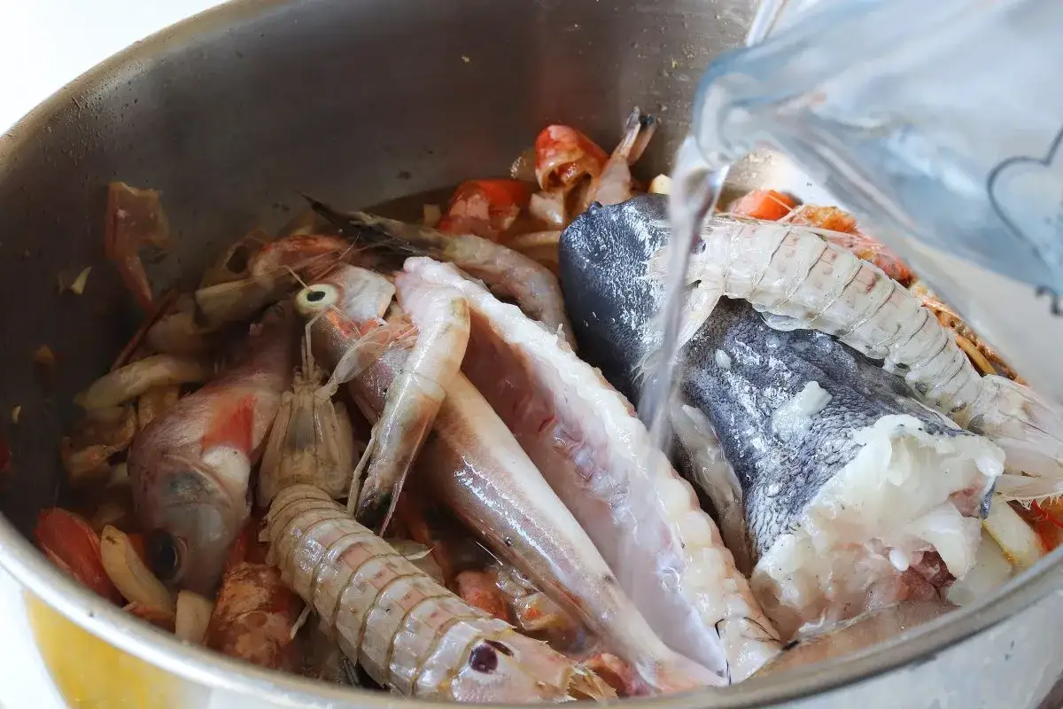 Agua cayendo sobre un bol lleno de gambas, pescado y otros mariscos, preparándose para un delicioso caldo de pescado.