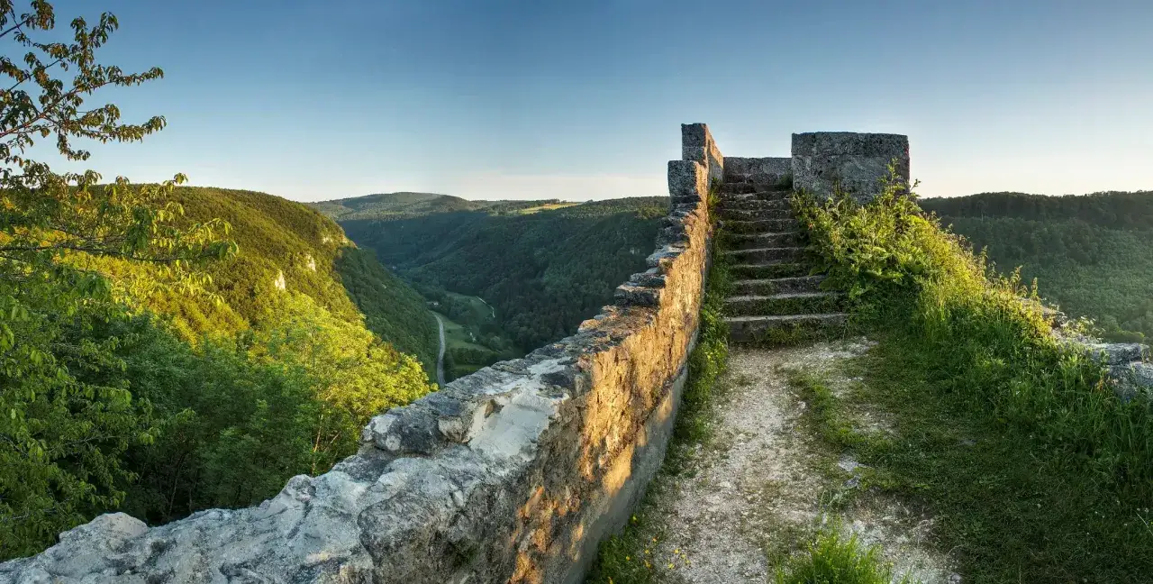 Sonnenbeschienene Ruinen der Burg Hohenwittlingen mit steinerner Mauer und Treppe, blicken auf ein grünes Tal.