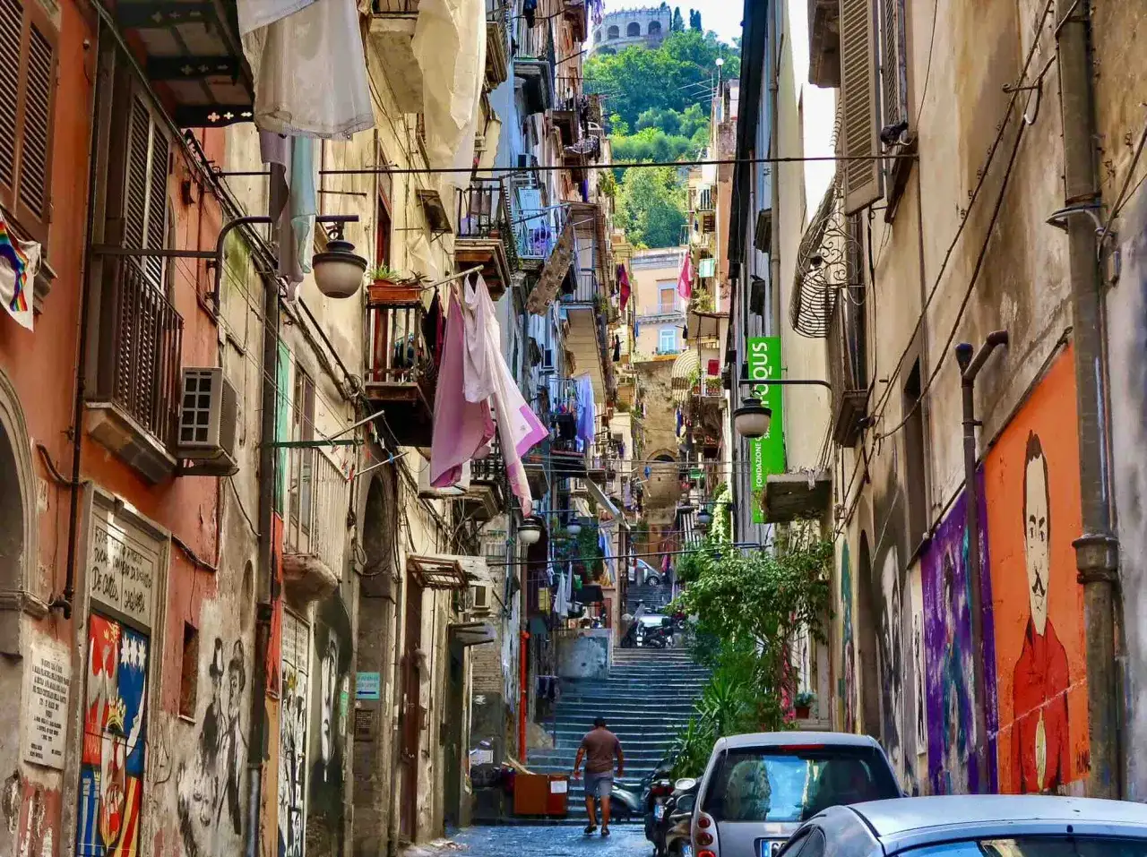 Un uomo cammina in un vicolo stretto di Napoli, con panni stesi e graffiti sui muri. Si percepisce il vero significato di 
