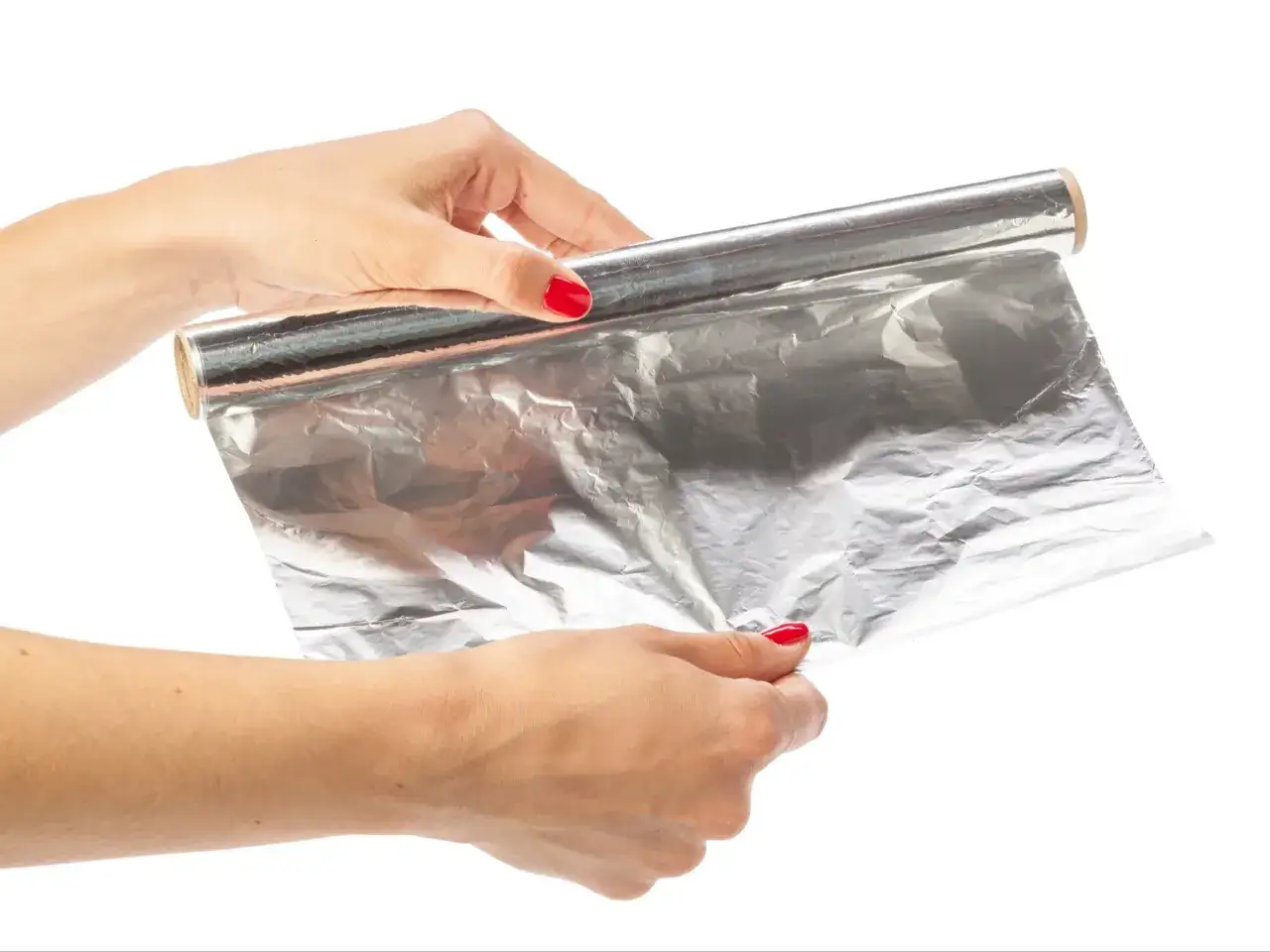 Dwie dłonie rozwijają rolkę folii aluminiowej, która błyszczy w świetle.