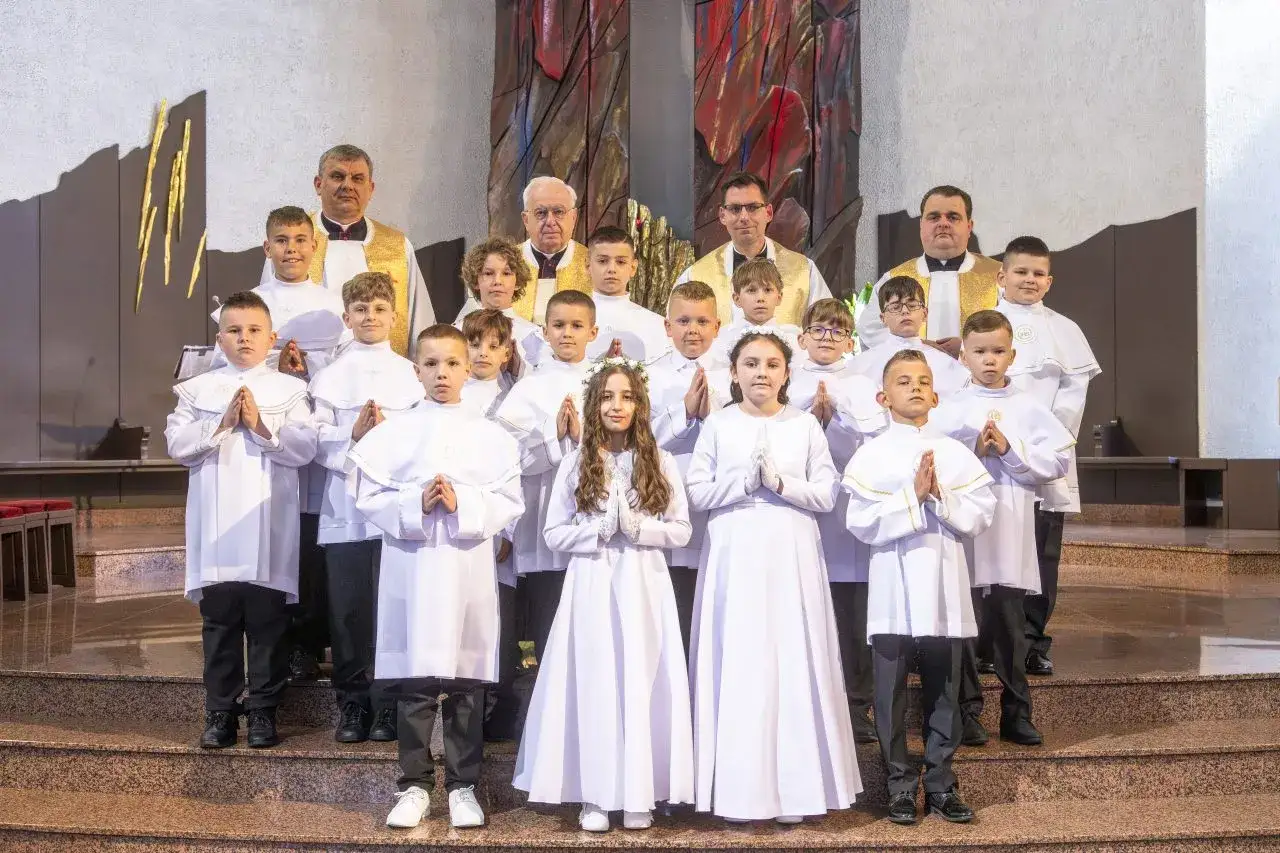 Dzieci w białych strojach komunijnych pozują do zdjęcia z księżmi. Zastanawiasz się, ile trwa komunia?