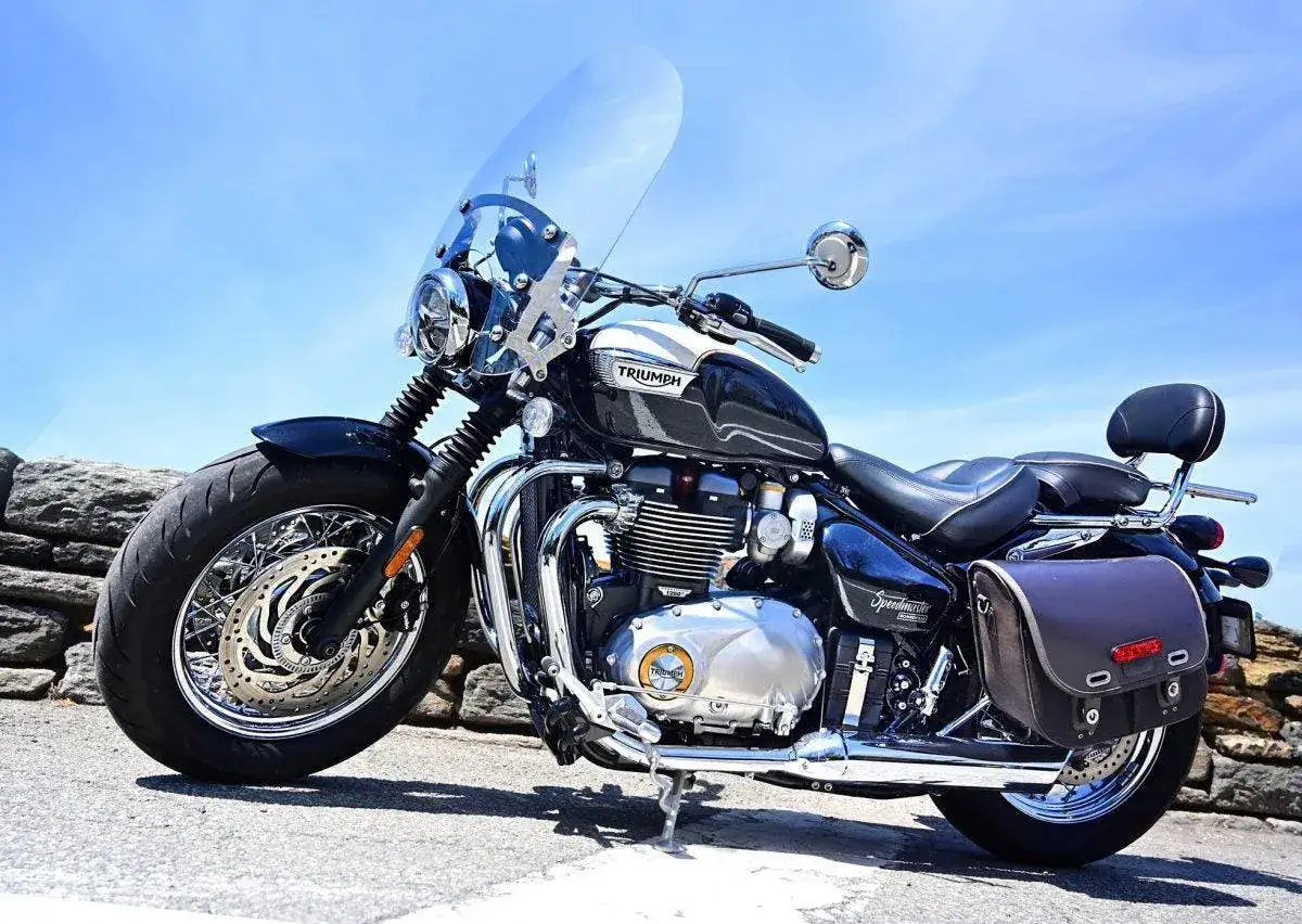 Czarny motocykl Triumph Speedmaster z dużą szybą i sakwami, gotowy na podróż.