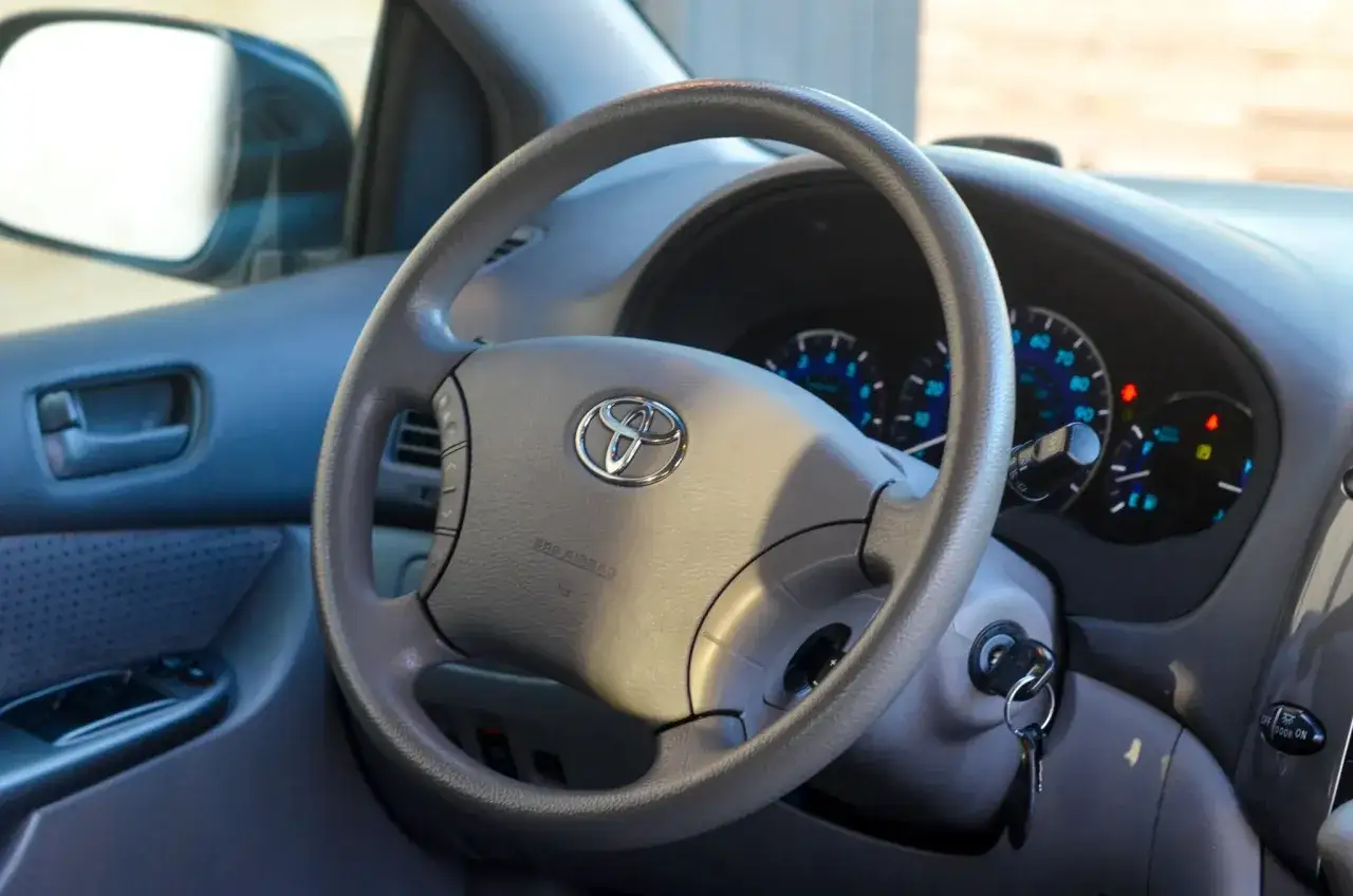 Wnętrze toyoty sienna hybrid: kierownica z logo, deska rozdzielcza z zegarami i kluczykami w stacyjce.
