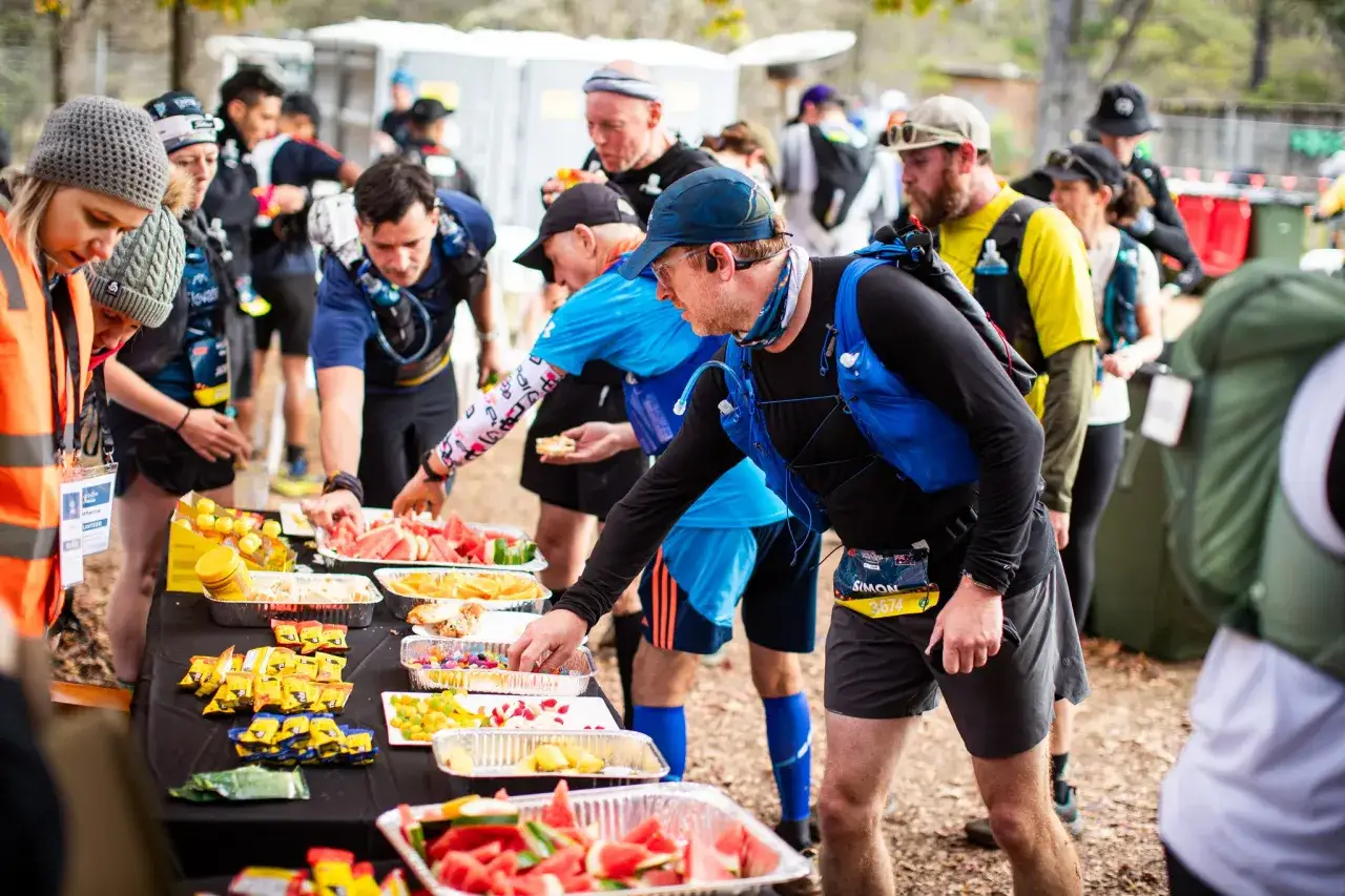 Läufer bedienen sich an einem Verpflegungsstand. Das ist typisch für einen Ultramarathon, wo Ausdauer und Ernährung entscheidend sind.