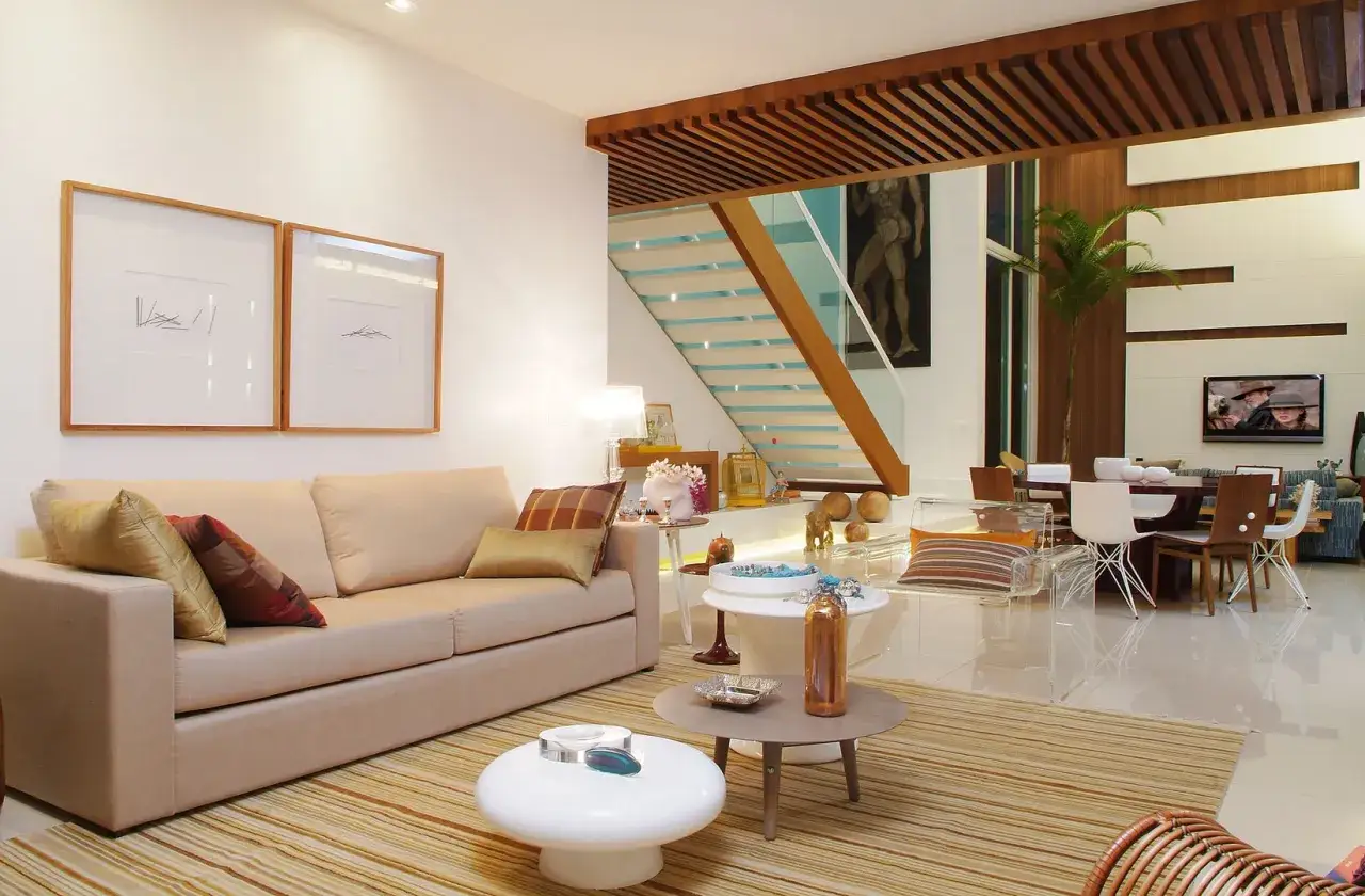 Elegantes salones marrones y beige con sof&aacute;, mesas auxiliares, alfombra de rayas y una escalera moderna.