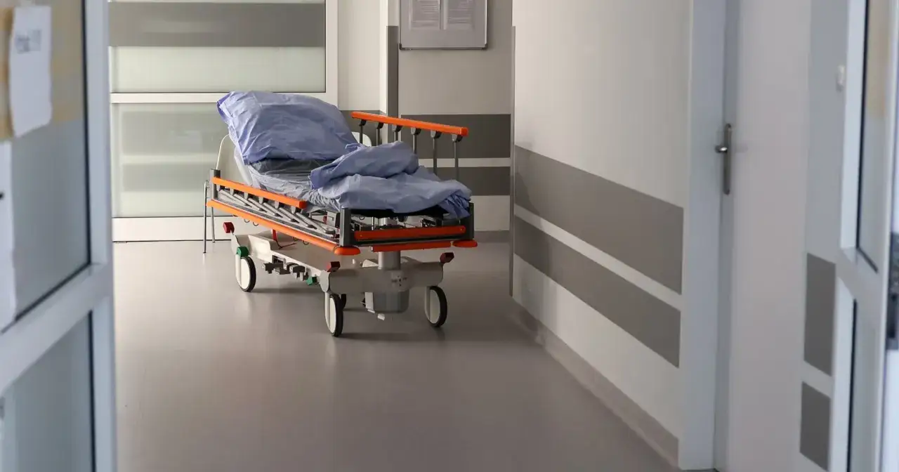 Pusty szpitalny łóżko na kółkach, przykryte niebieską pościelą, stoi na korytarzu. Czy szpital informuje o zgonie w nocy?
