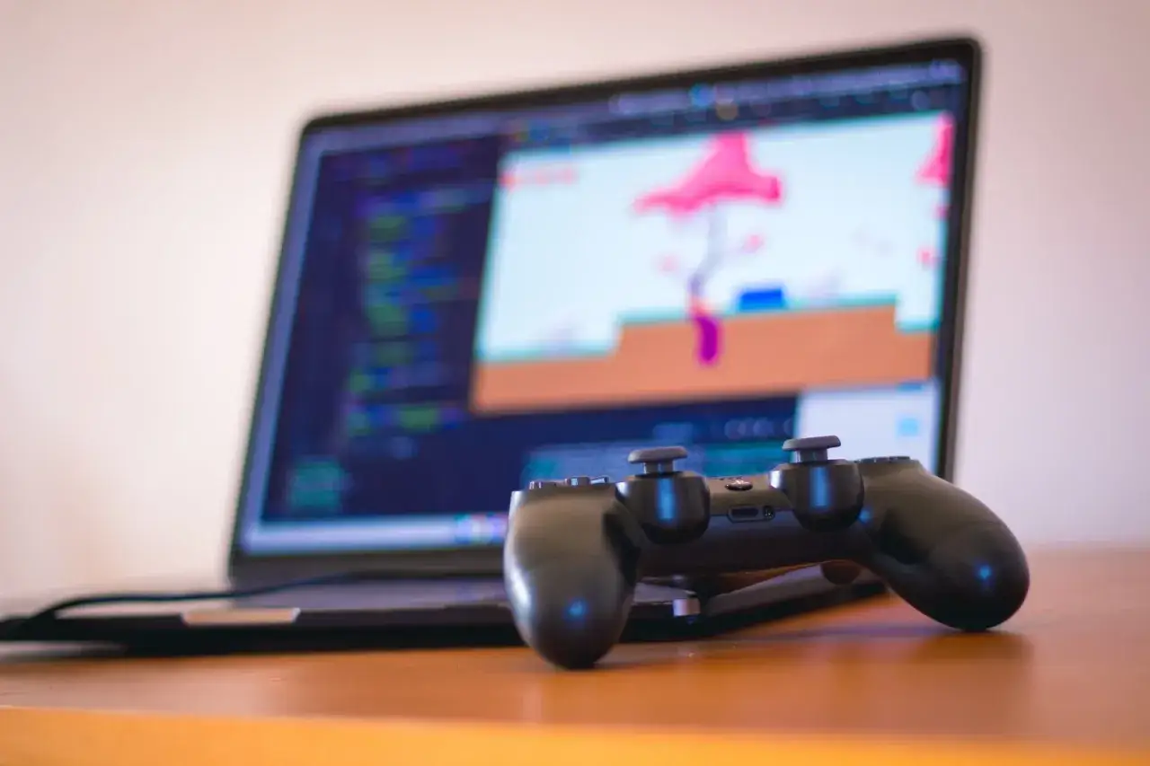 Kontroler PS4 leży przed laptopem z kodem i grą na ekranie. Dowiedz się, jak podłączyć PS4 do laptopa, aby grać na większym ekranie.