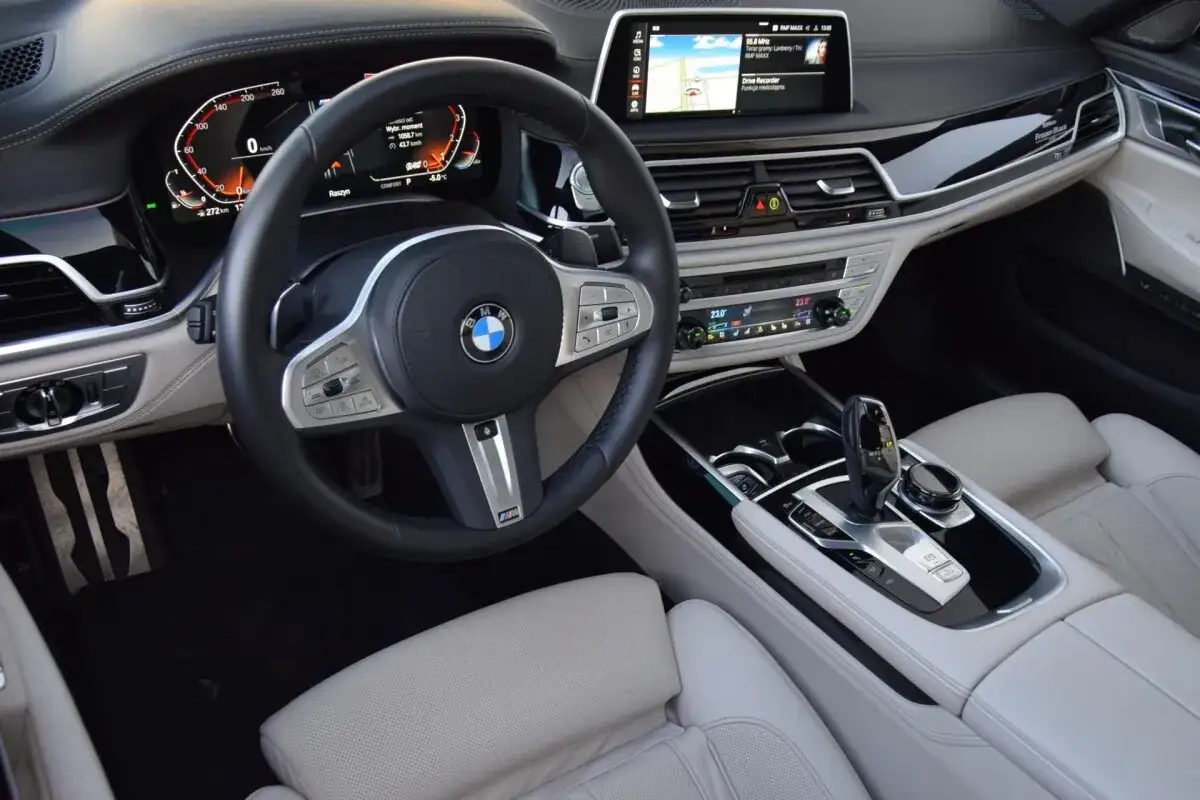 Wnętrze BMW 750i: skórzana tapicerka, cyfrowe zegary, ekran multimediów i elegancka konsola środkowa.